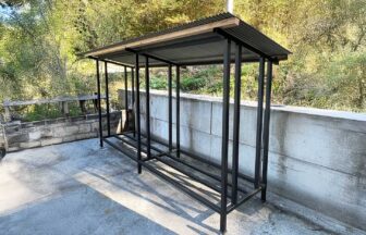 黒いスチール製フレームと屋根が付いた2ブロック構造の屋外用薪棚